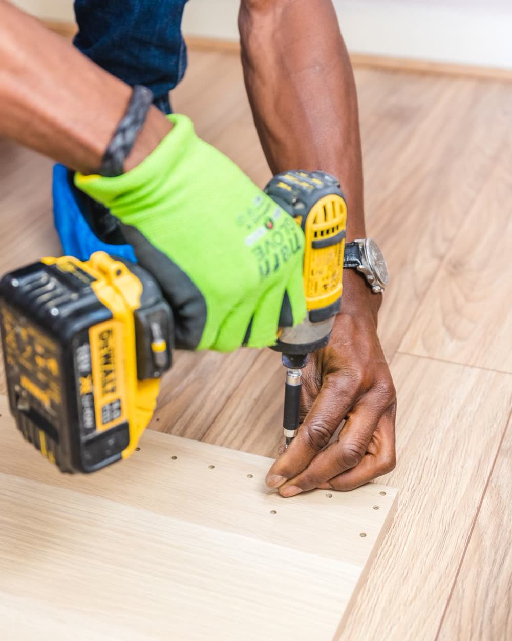 Gloved hands driving a screw into a wooden panel with a cordless drill