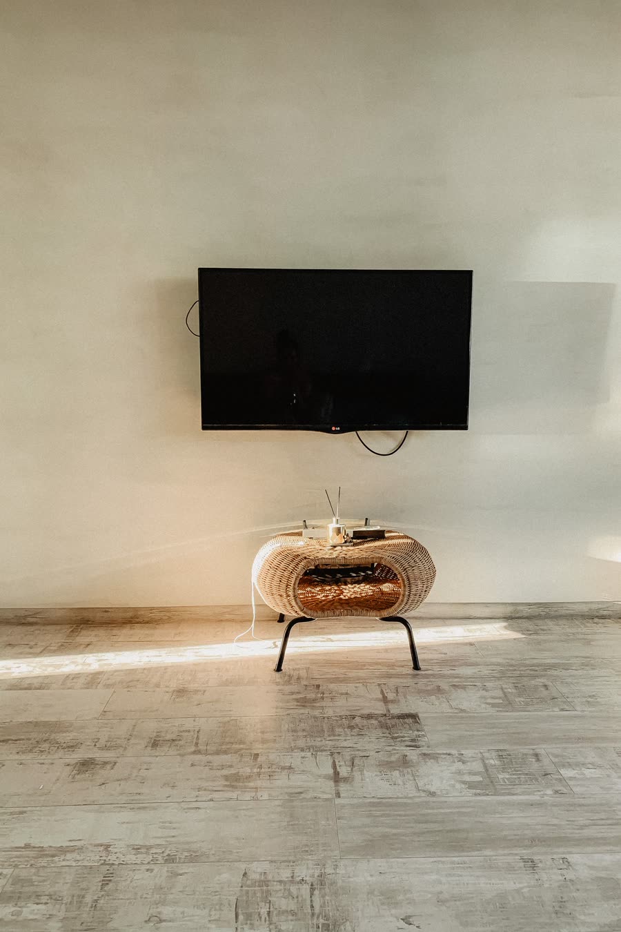 A flat-screen television mounted on a warm plaster wall above a woven side table