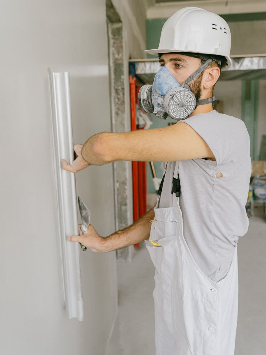 A worker drawing a wide trowel of filler down a bare interior wall