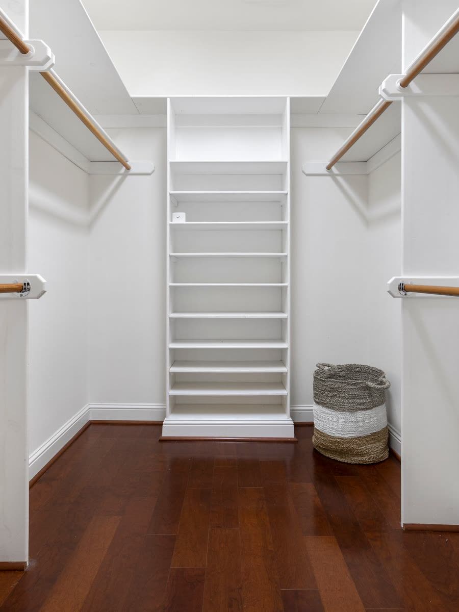 A fitted walk-in closet with white shelving and hanging rails over dark wood flooring